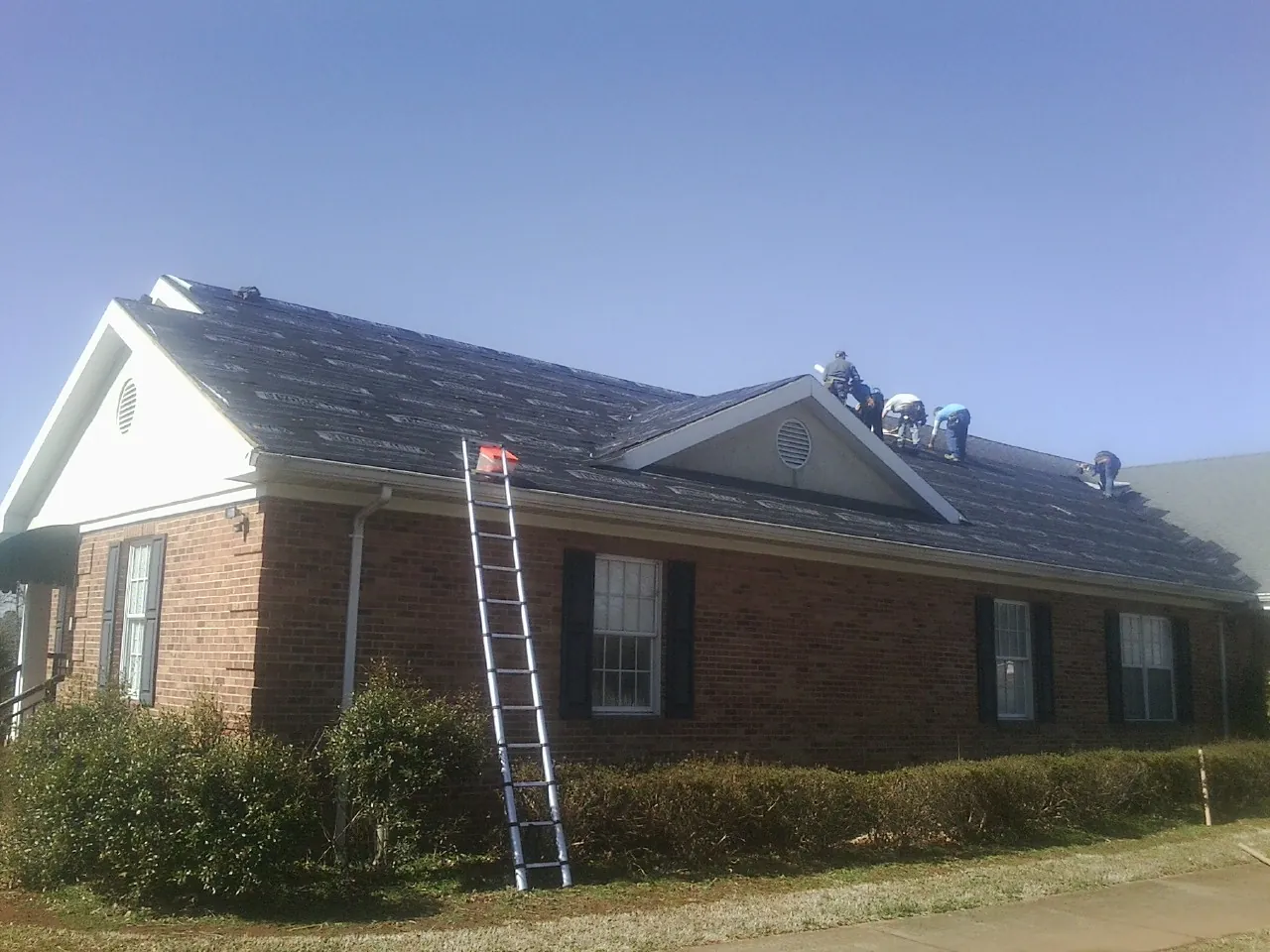 Crew tearing shingles off a brick ranch roof with a ladder set — Metal Roof Repair work by our crew in Grove City