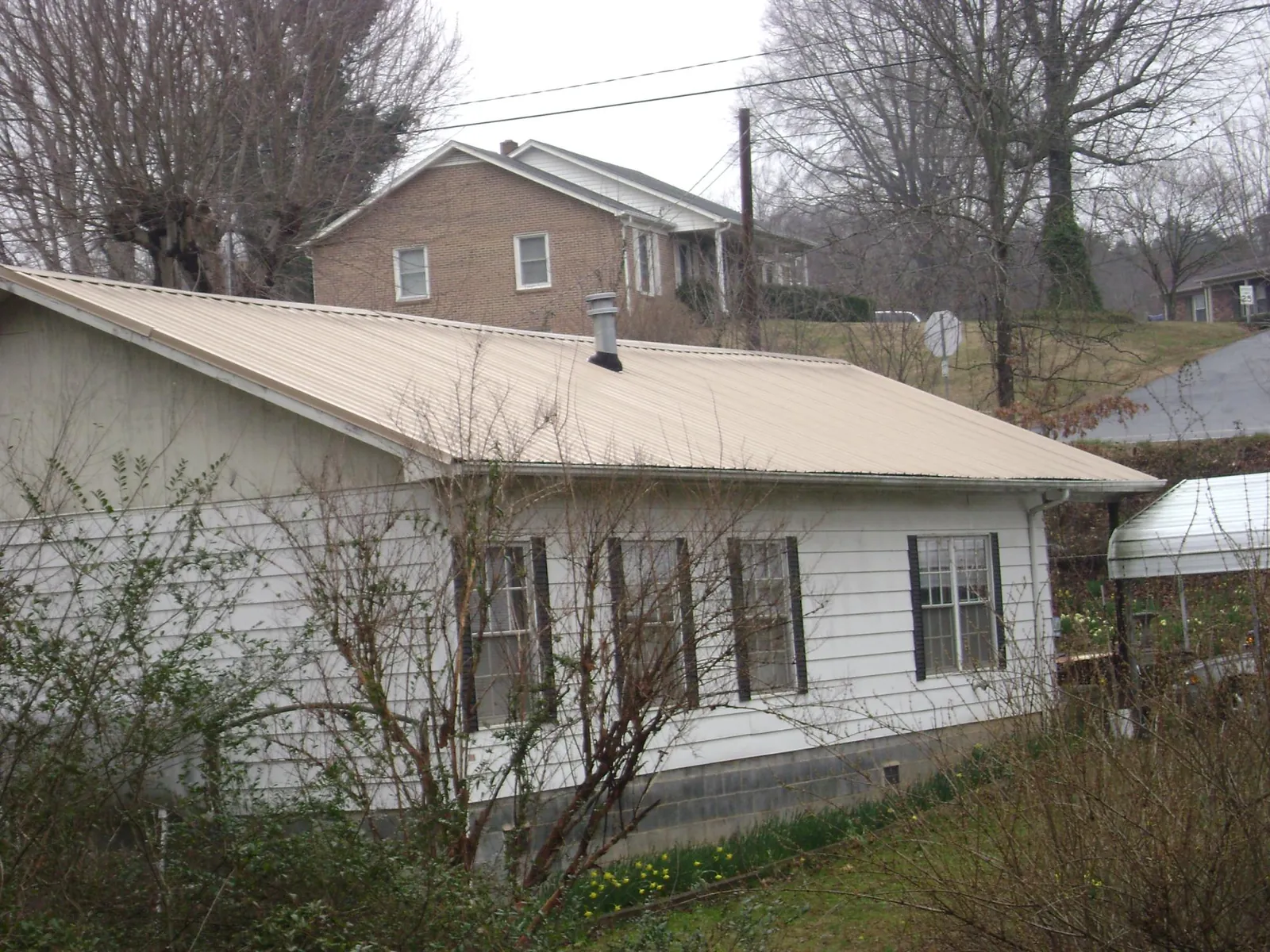 Tan metal roof on a white sided house set into a hillside — Commercial Roofing by Roofing Brothers in Grove City